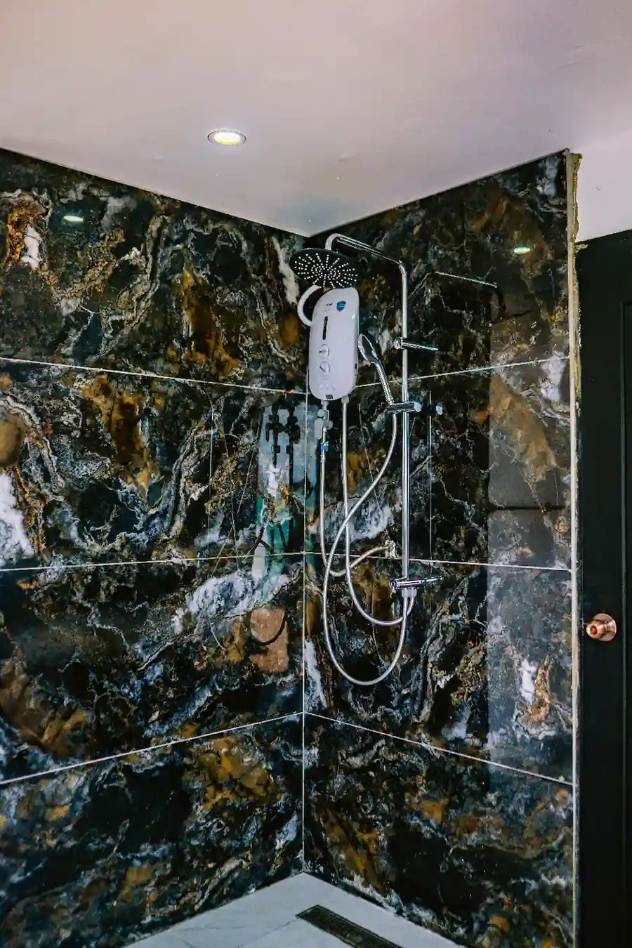 Modern corner shower with dark marble-style tiles inside the Family Deluxe room at Turtle Seaweed Resort.